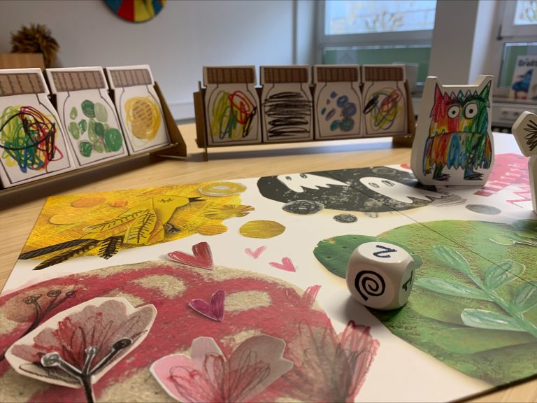 Ein Würfelspiel steht aufgebaut auf einem Holztisch mit selbstgemalten Spielfiguren